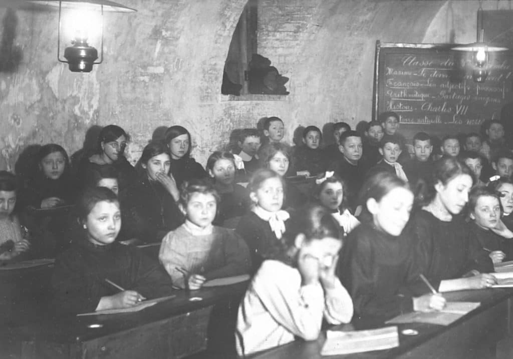 École sous occupation : classe dans une cave pendant la guerre, tableau noir et enfants aux pupitres, 1914-1918