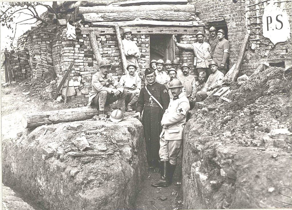 Médecins et infirmiers Grande Guerre groupés devant l'entrée d'un poste de secours à Lihons en septembre 1916, aumônier en soutane au premier plan