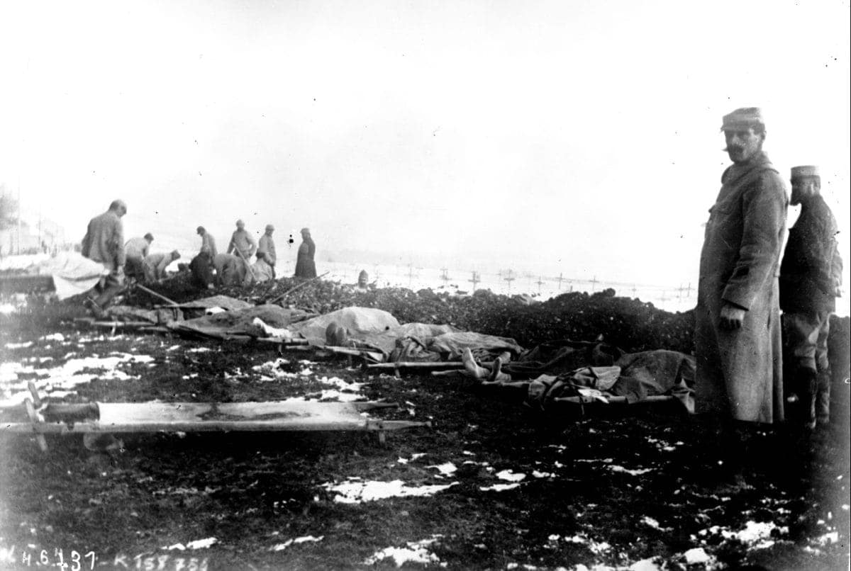 Brancardiers français inhumant des soldats sur le champ de bataille près de Verdun, avec dépouilles enveloppées sur des brancards et alignement de croix de bois en arrière-plan, hiver 1916.
